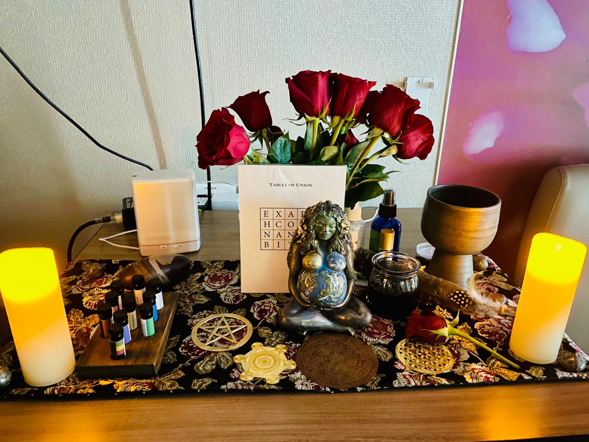 The image includes an altar created for the birth and blessing of baby Margo. The altar contains roses, a statue of Mother Gai, and offerings for each of the directions and elements of the earth.